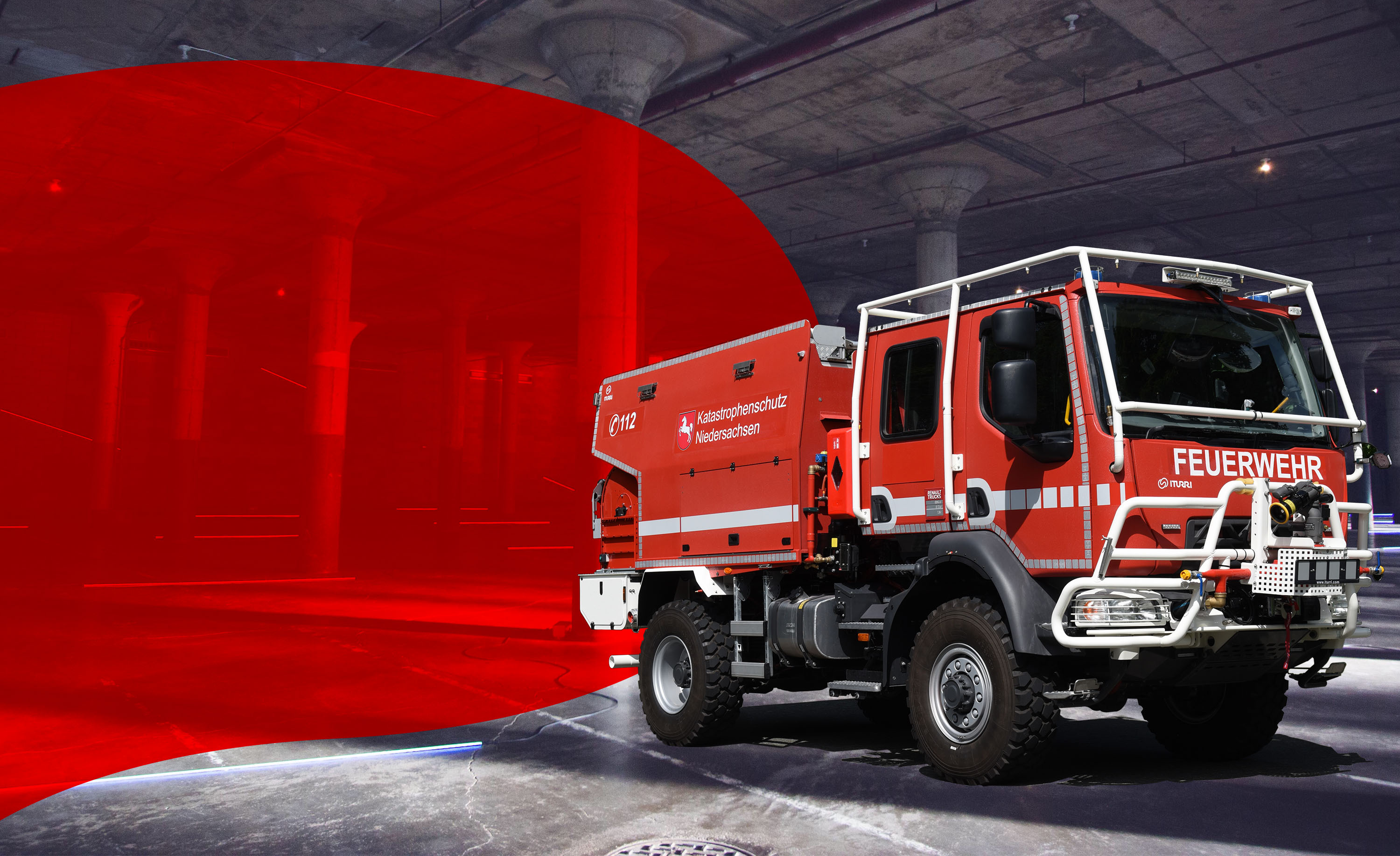 rotes Feuerwehrfahrzeug fährt auf einer Strasse mit einer Stadt im Hintergrund, von der linken Seite ragt eine rote Fläche in das Bild